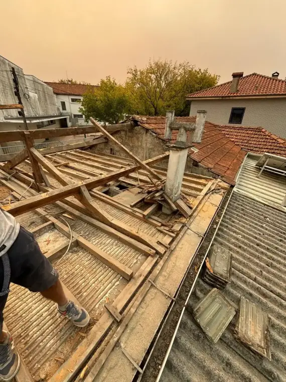 Charpente bois mise à nu en pleine dépose : chevrons, pannes et liteaux anciens en bois brut démontés et empilés en désordre autour d'une souche de cheminée.